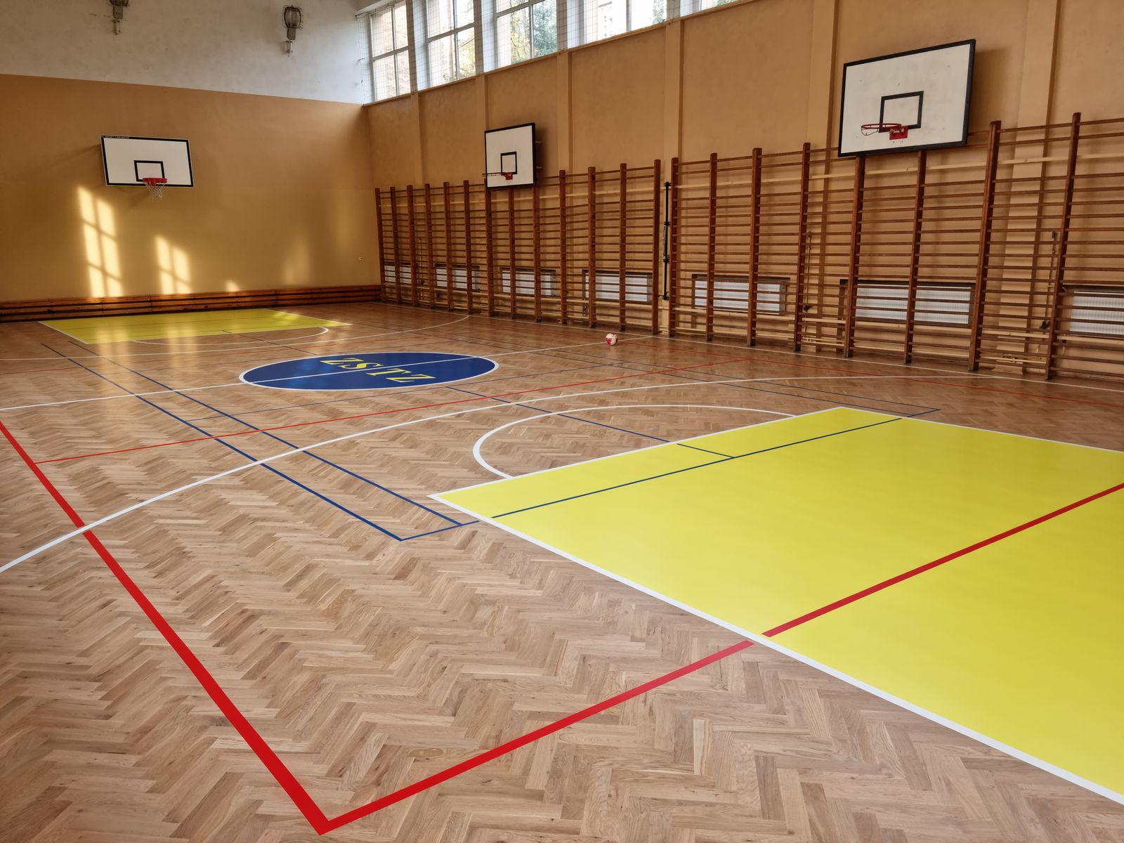 Szkolna sala gimnastyczna z dębową jodełką i malowanymi liniami boisk – realizacja Perfekt Parkiet