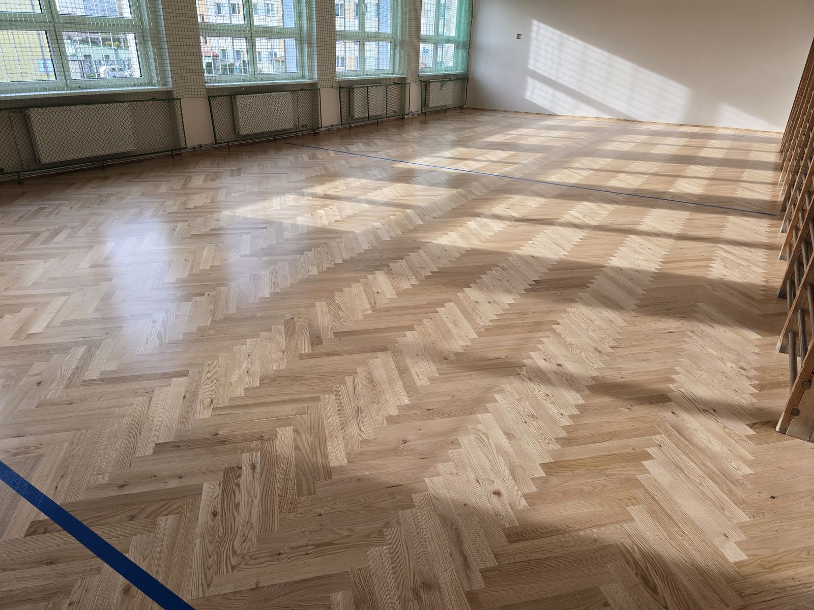 Dębowa jodełka w szkolnej sali w porannym słońcu – realizacja Perfekt Parkiet